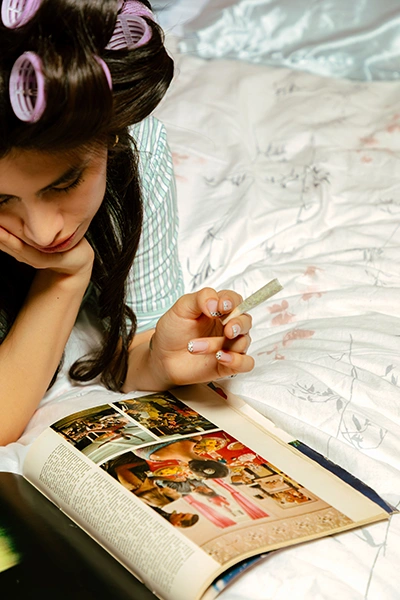 A person lying on their bed and reading while smoking cannabis
